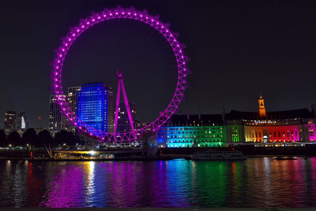 Vibrant night view of the London Eye with colorful lights reflecting on the Thames River.