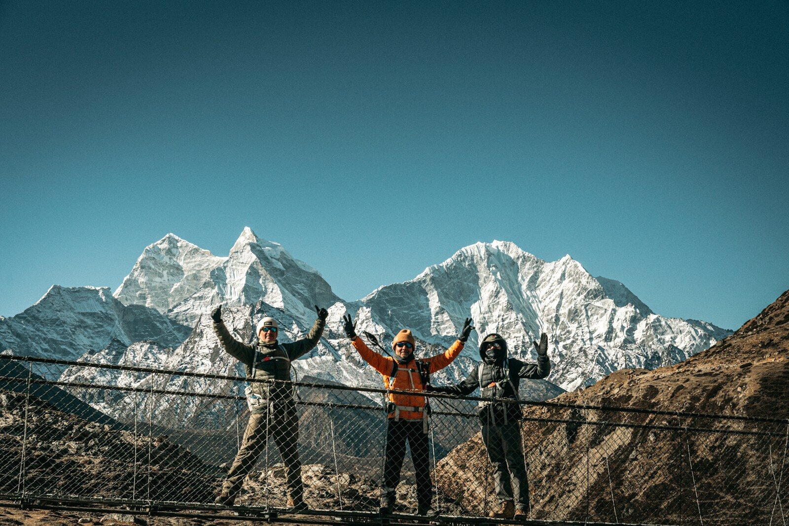 Three hikers celebrate on a suspension bridge with mountains